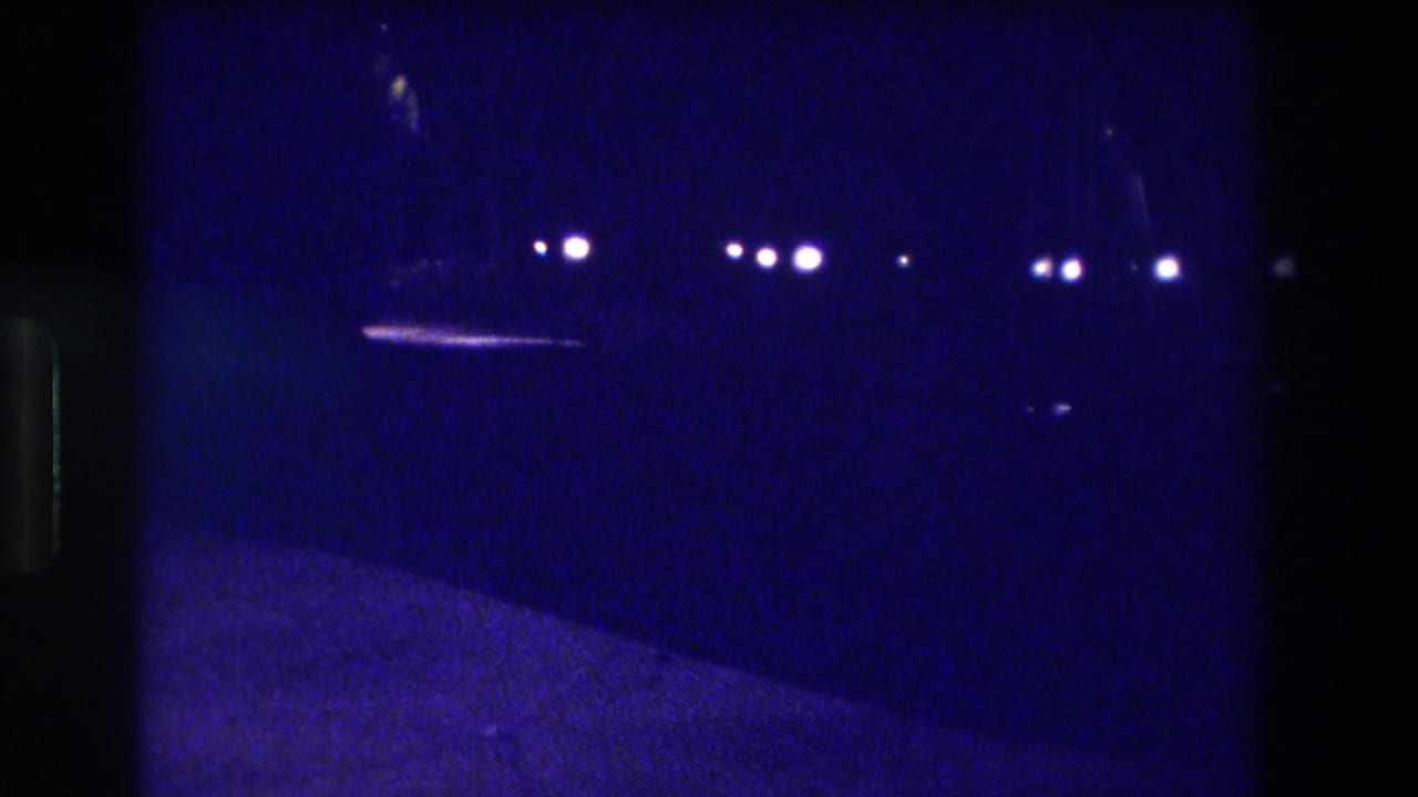 8mm home movie frame circa 1982, likely Acapulco — blue-indigo color cast with multiple distant streetlights and probable vehicle lights in near-darkness.