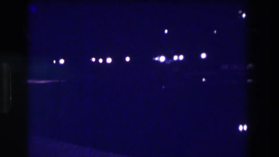 Low-light 8mm frame circa 1982, likely Acapulco — clusters of out-of-focus streetlights and probable vehicle headlights punctuate deep blue darkness.