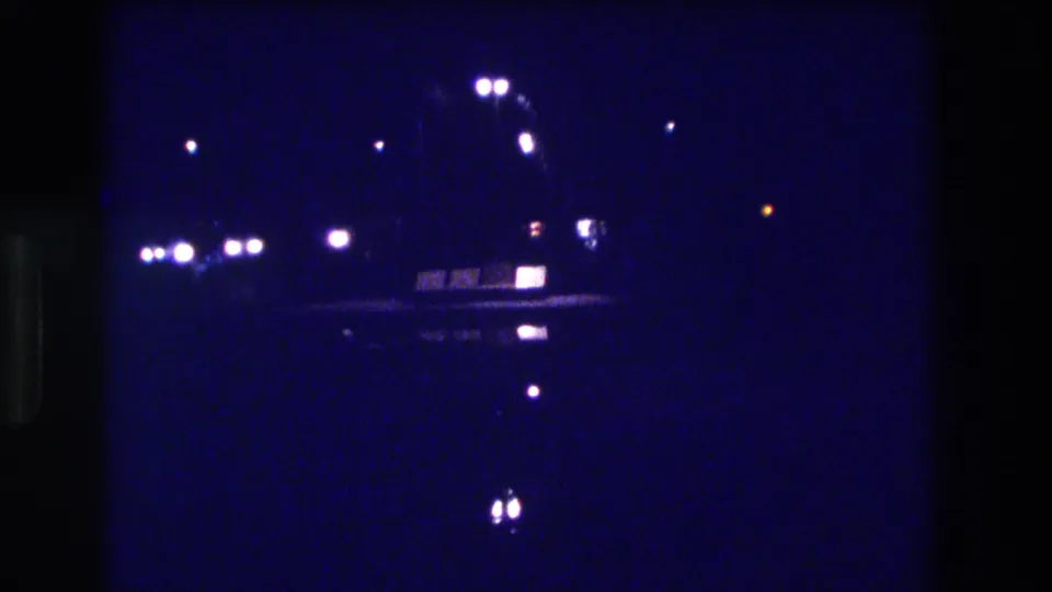 8mm frame circa 1982, likely Acapulco — blue-tinted night lights with one orange-toned point source and an unidentified pale shape visible near the lower frame.
