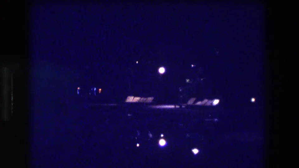 8mm home movie frame, Acapulco Mexico 1982 — dark coastal night with scattered shoreline lights and a bright horizontal band from what may be an elevated roadway or structure.