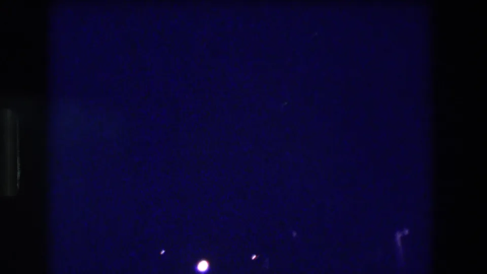 Extremely underexposed 8mm night frame from Acapulco, 1982 — almost entirely dark blue with one dominant point light source visible.