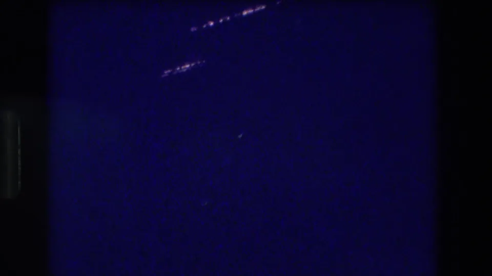 8mm night footage, Acapulco 1982 — a diagonal band of lights from a distant elevated structure crosses the upper frame over dark coastal water.