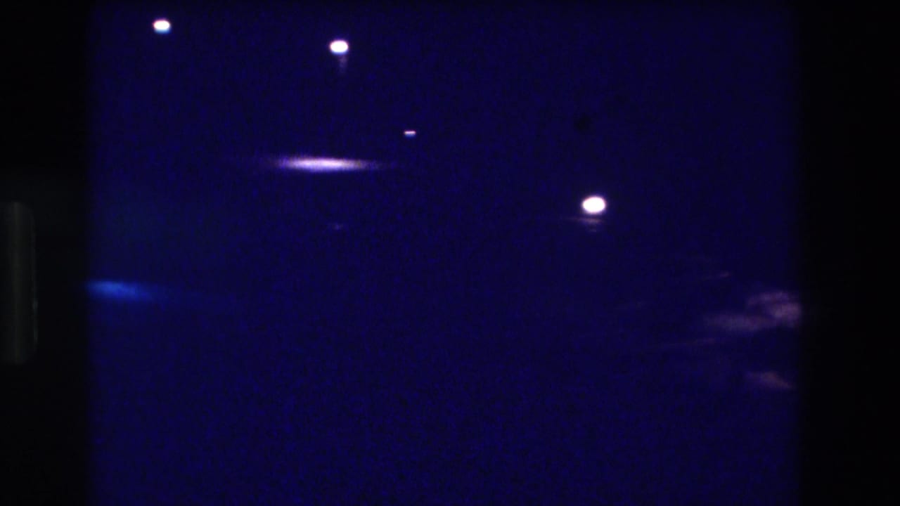 8mm night pan, Acapulco Mexico 1982—nearly dark frame with scattered pinpoint lights and a faint shape at the right edge; the glowing area from the opening has moved out of view.