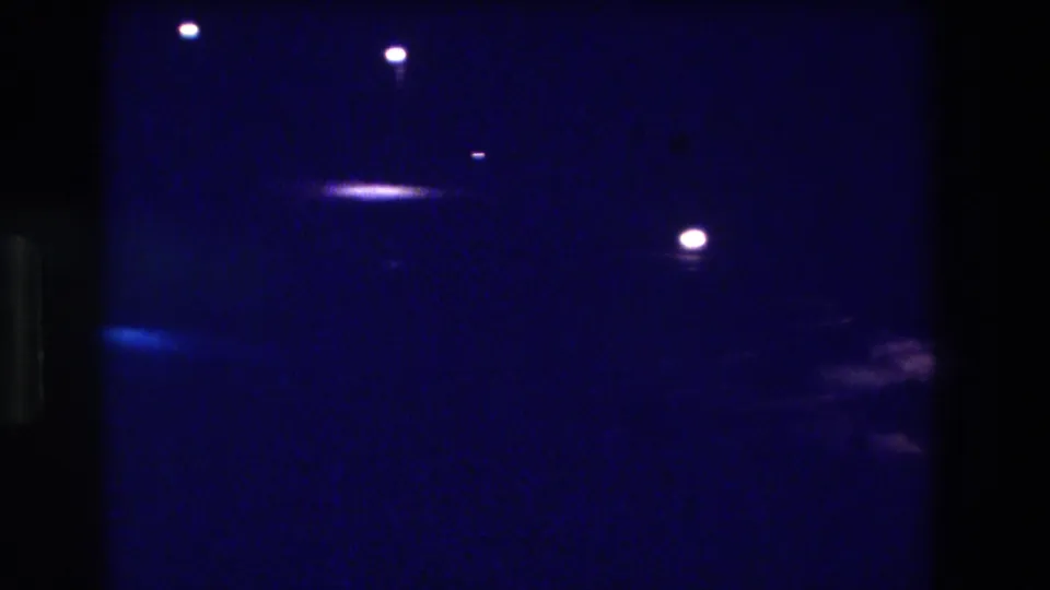 8mm night pan, Acapulco Mexico 1982—nearly dark frame with scattered pinpoint lights and a faint shape at the right edge; the glowing area from the opening has moved out of view.