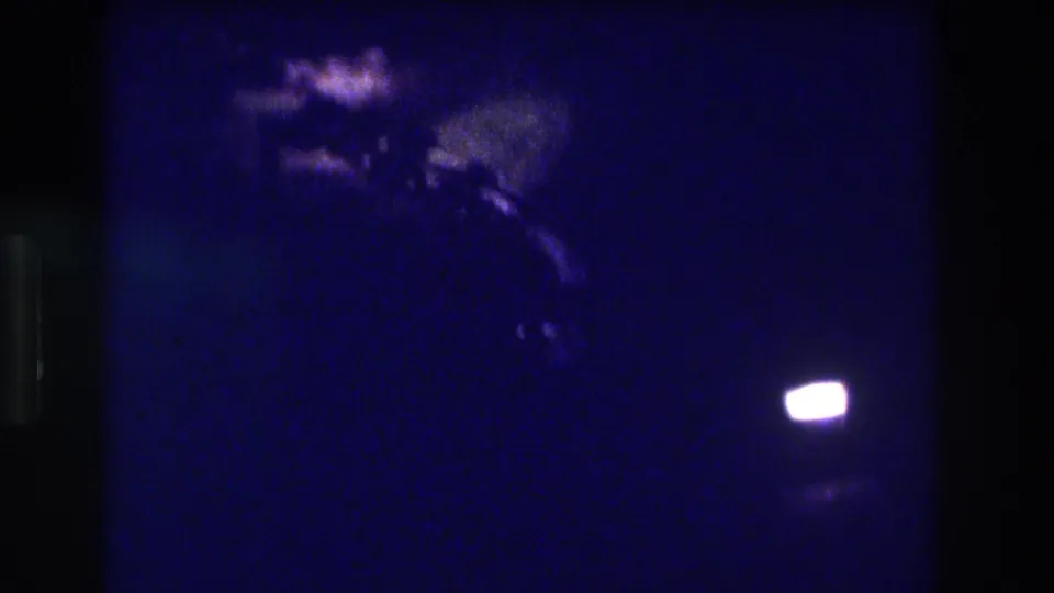8mm night pan, Acapulco Mexico 1982—indistinct blurry shapes at center-right and a bright oval light at lower right, possibly a vehicle headlight or street lamp.
