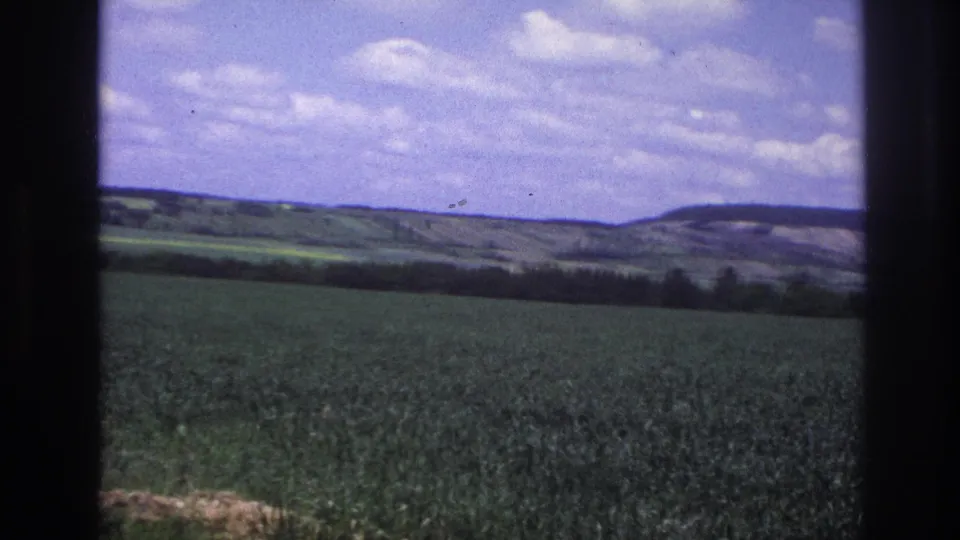 8mm home-movie frame from France, c.1967 — sky fills more of the frame as the vehicle angle shifts, revealing a wide-open agricultural landscape with low rolling hills.