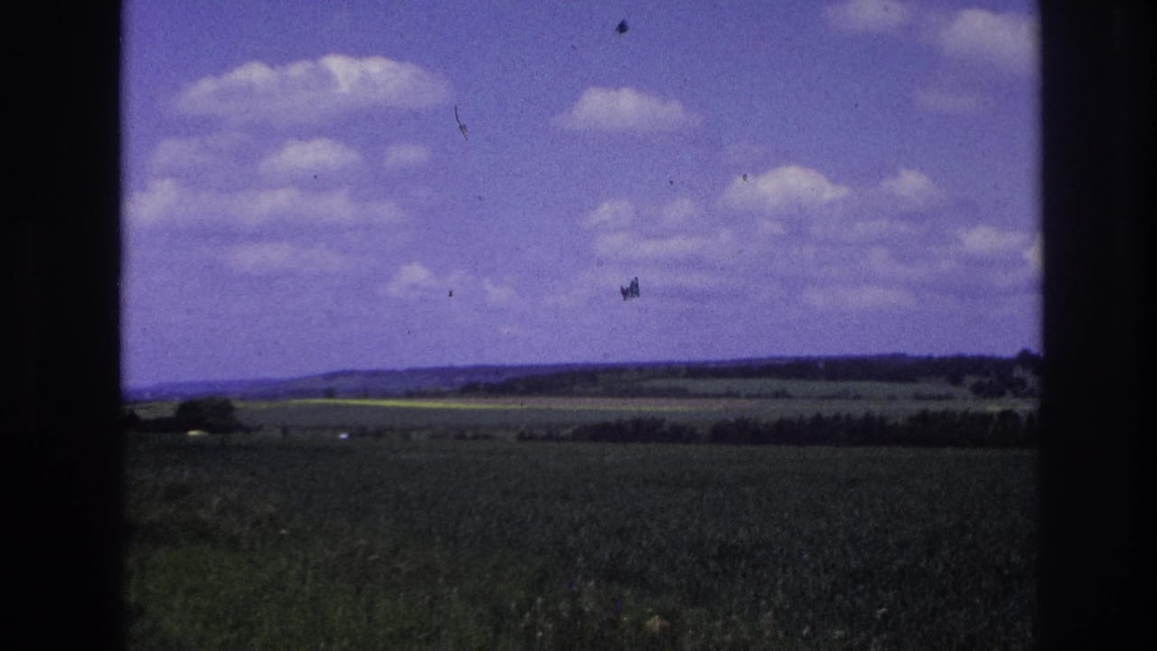 Green fields and distant hills under a blue sky with clouds, seen through dark film frame edges.