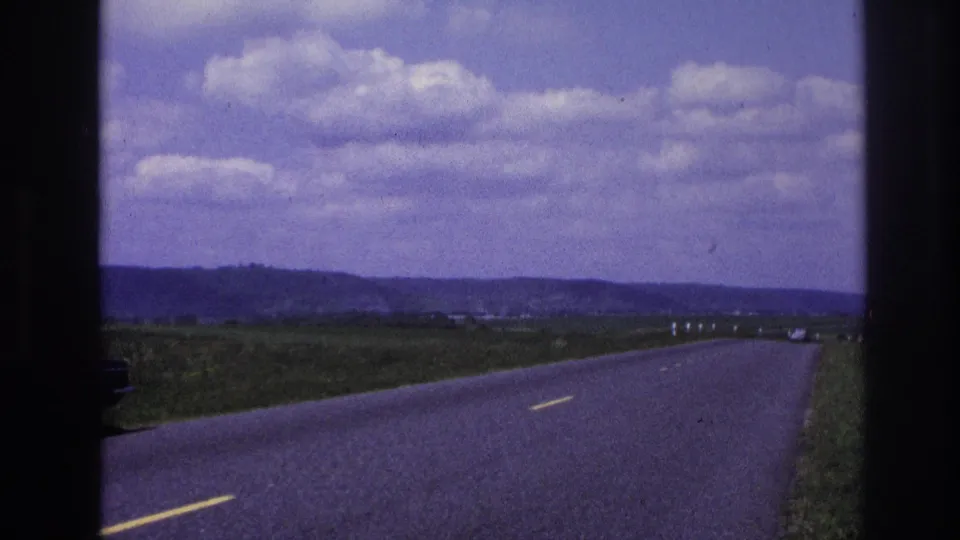 Final 1967 France 8mm frame with the road stretching across open countryside toward low hills as a yellow truck recedes near the horizon.