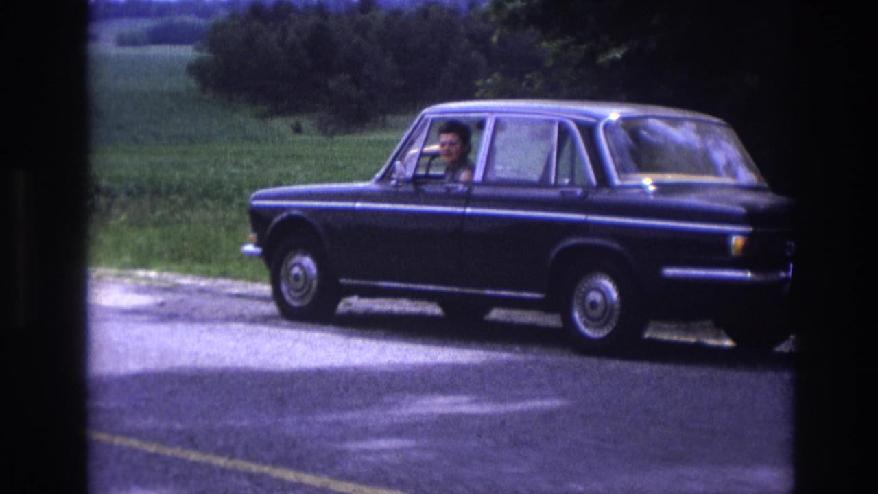 Mid-1960s European sedan on a French rural road, driver more visible through window, chrome wheel covers and body trim evident in this 8mm frame from 1967.