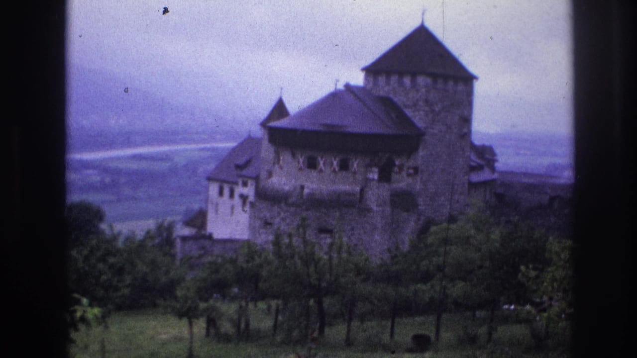 8mm home-movie frame from France, 1967, showing a stone fortified castle with dark pyramidal roofs above a broad hazy valley under overcast sky.