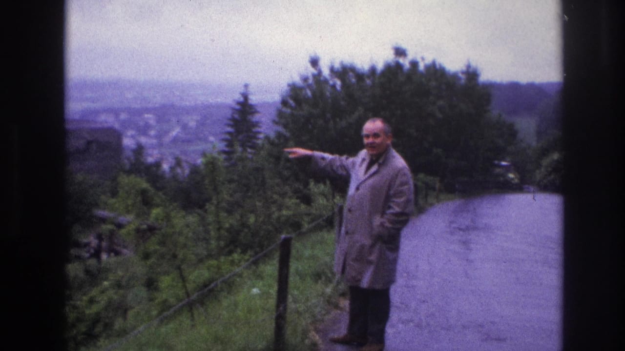 Slightly closer view of man in light overcoat gesturing toward an off-screen landmark on a winding hillside road, France, circa 1967.