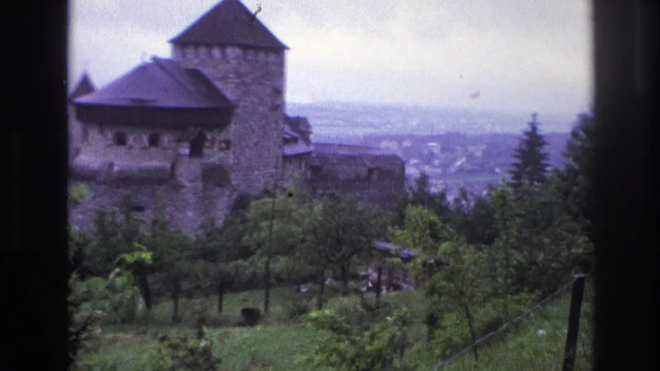 Medieval stone castle with round tower and dark conical roof on a French hillside, circa 1967, 8mm footage showing characteristic blue color shift.