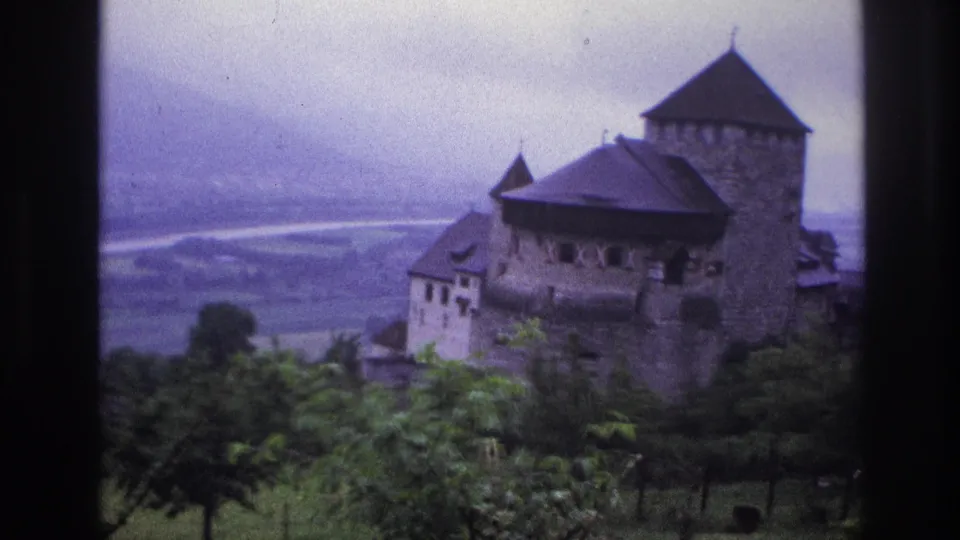Medieval castle on French hillside, circa 1967, showing round tower with dark roof and broad river valley below, 8mm home movie footage.