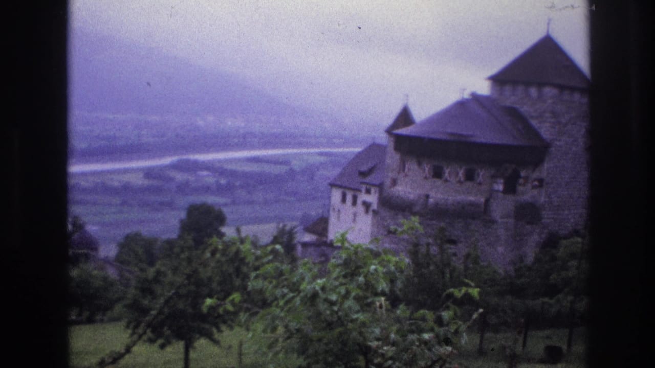 8mm home movie frame from France, circa 1967, stone castle with conical peaked roof and white rendered tower, vineyard trees in foreground, hazy valley beyond.