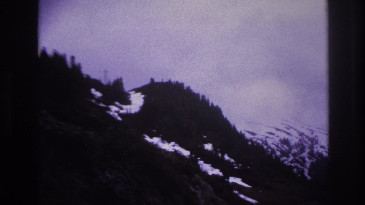 Aged 8mm film frame showing snow-covered alpine peaks under a moody overcast sky, likely French Alps, 1967.