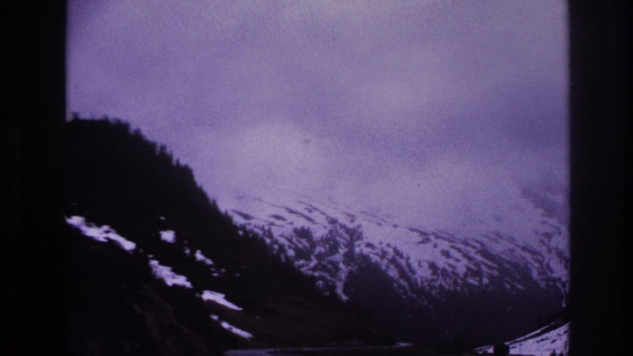 Snow-covered alpine slope and overcast sky seen from a moving vehicle, with a purple 8mm color cast.