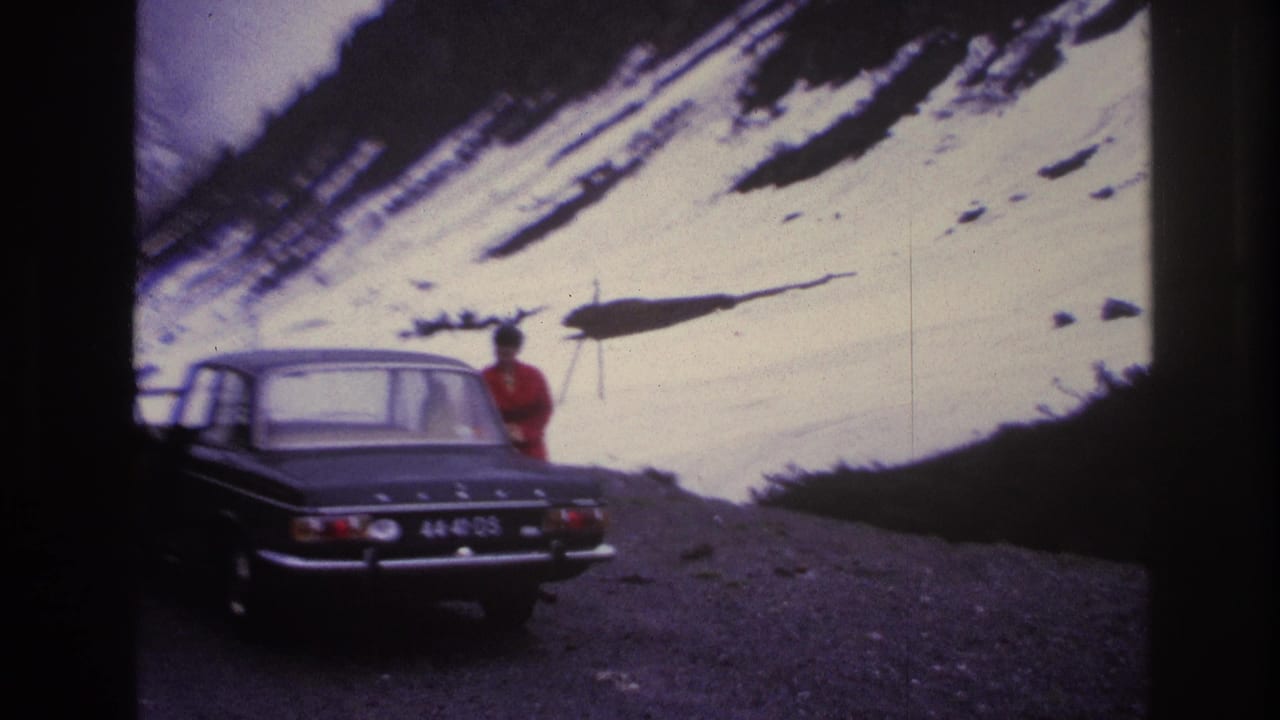 Woman in red coat approaching the rear door of a dark European sedan on a French mountain road, c.1967, with a steep snowy slope and overcast sky in the background.