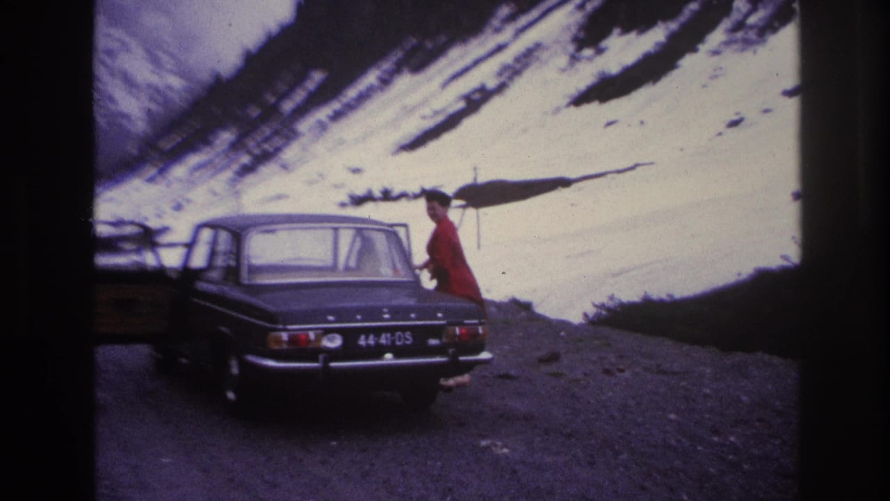 Woman in red coat opening the rear passenger door of a dark 1960s sedan, snow-covered mountain slope visible behind.