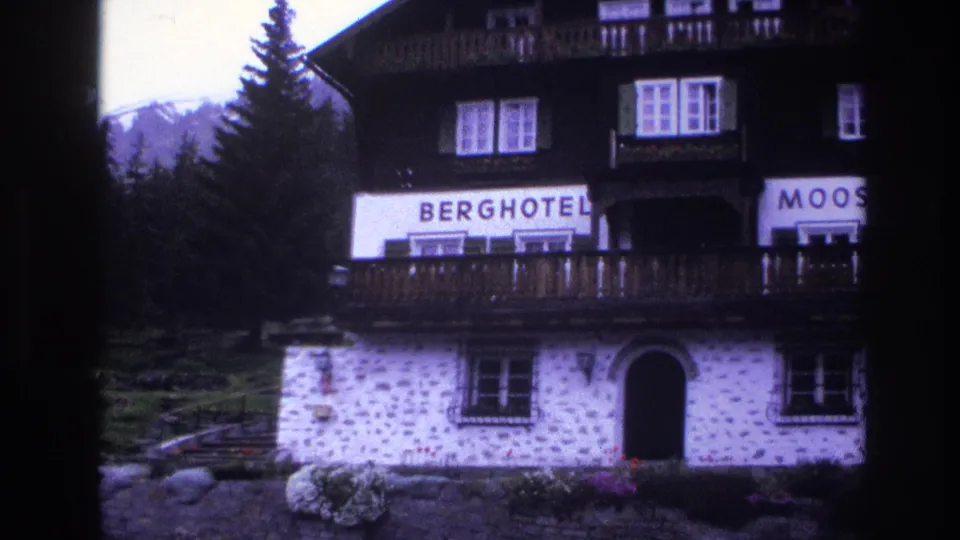 Alpine Berghotel showing BERGHOTEL and partial MOOS signage, dark wood upper story over stone masonry, flower planters at base, circa 1967 France, 8mm film.