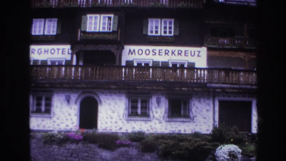 Full-height facade of Berghotel Mooserkreuz, c.1967, from arched stone entrance at ground level to dark timber upper floors; flower boxes and sign banners clearly visible; purple 8mm cast.