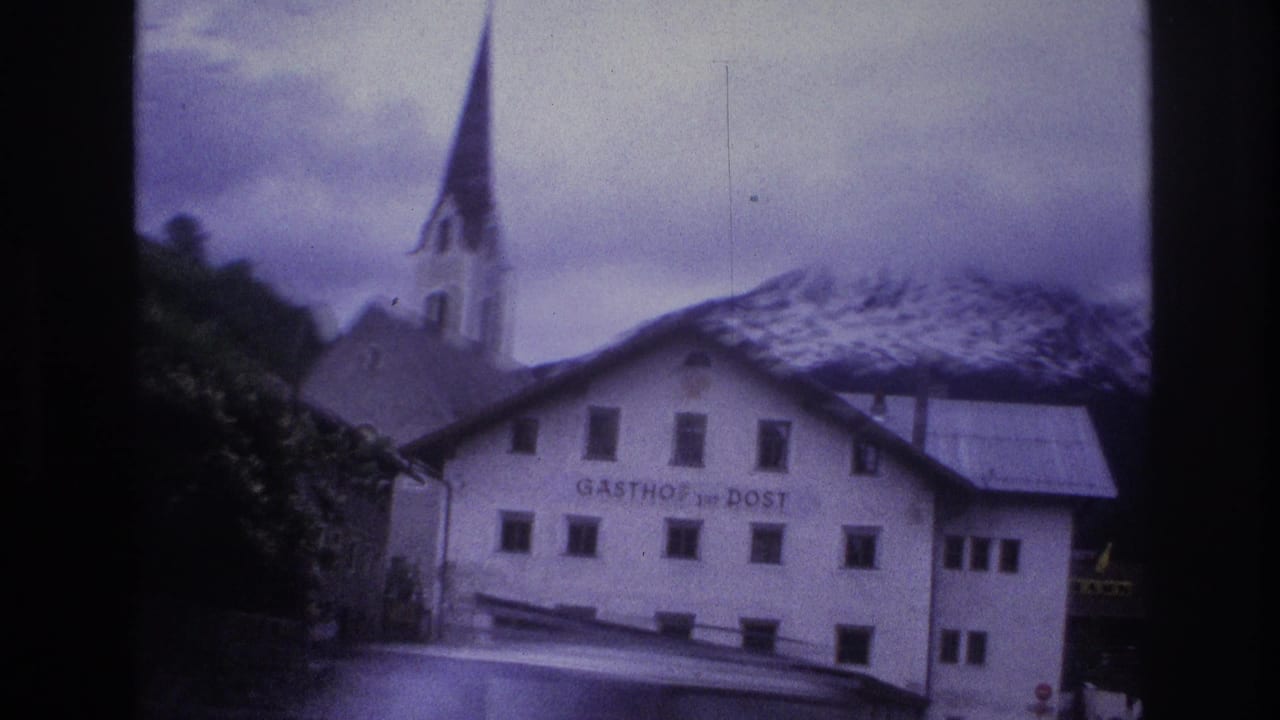 White 'GASTHOF zur POST' inn and church steeple against snow-capped Alpine peaks, 8mm home movie circa 1967 with blue-purple dye shift.