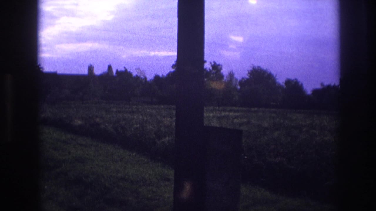 1967 France 8mm home movie — rural meadow seen through a window at dusk, deep purple sky with intense light flare and silhouetted trees.