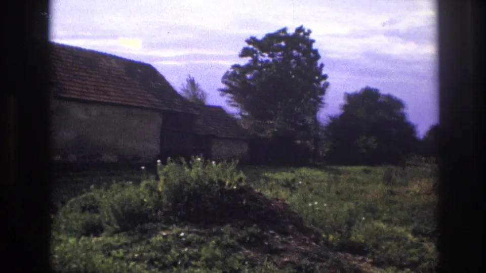 1967 France 8mm view of a rustic countryside house with a tiled roof, garden growth, trees, and dark film borders.