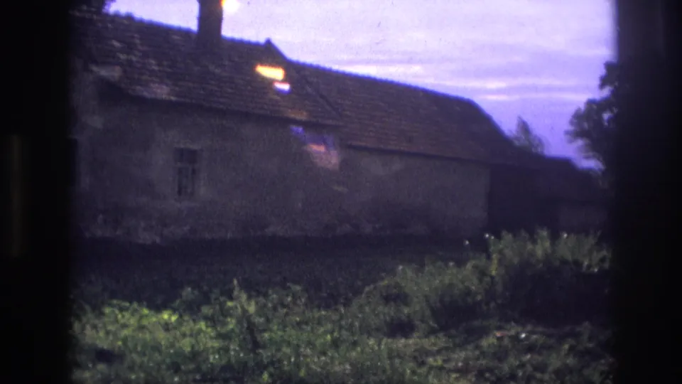 1967 France 8mm frame with a closer exterior angle on the house wall, tiled roof, small window, grass, and plants.