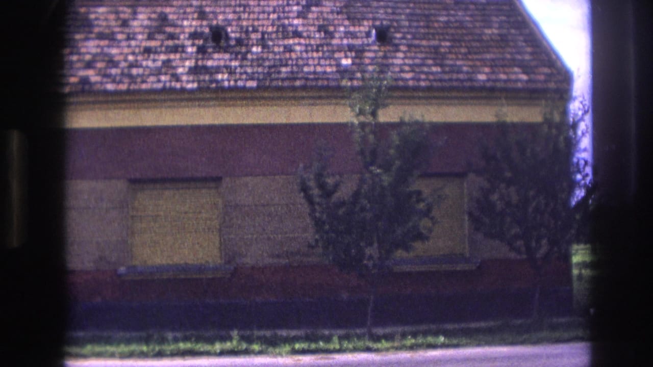 1967 France 8mm frame showing a street-facing red and yellow house with boarded windows, a brown tiled roof, and small front trees.