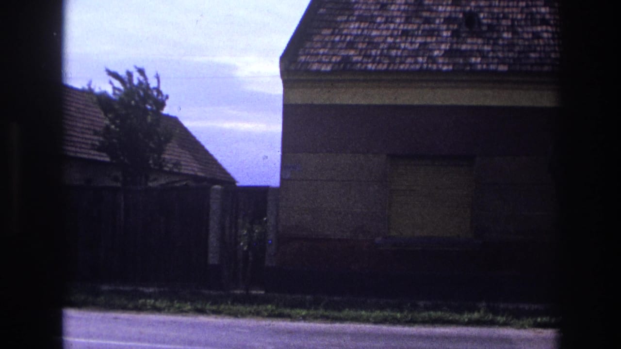 1967 France home-movie frame showing a shuttered house with tiled roof beside a quiet roadside.