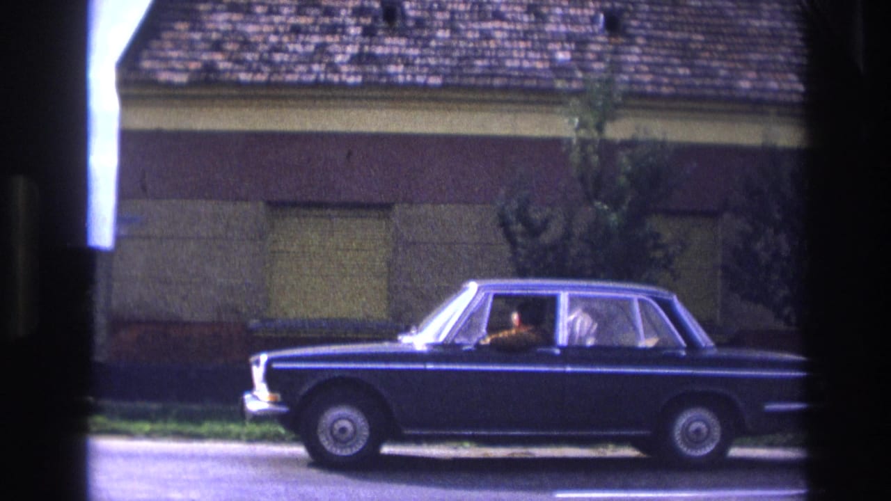 Dark blue sedan centered beside a building with shuttered windows.