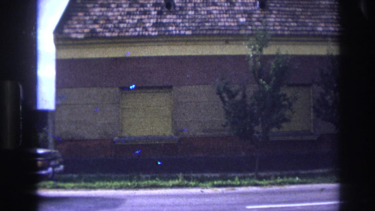 1967 France 8mm frame showing a black sedan near a yellow stucco house, shuttered windows, sidewalk, and dark scan edges.