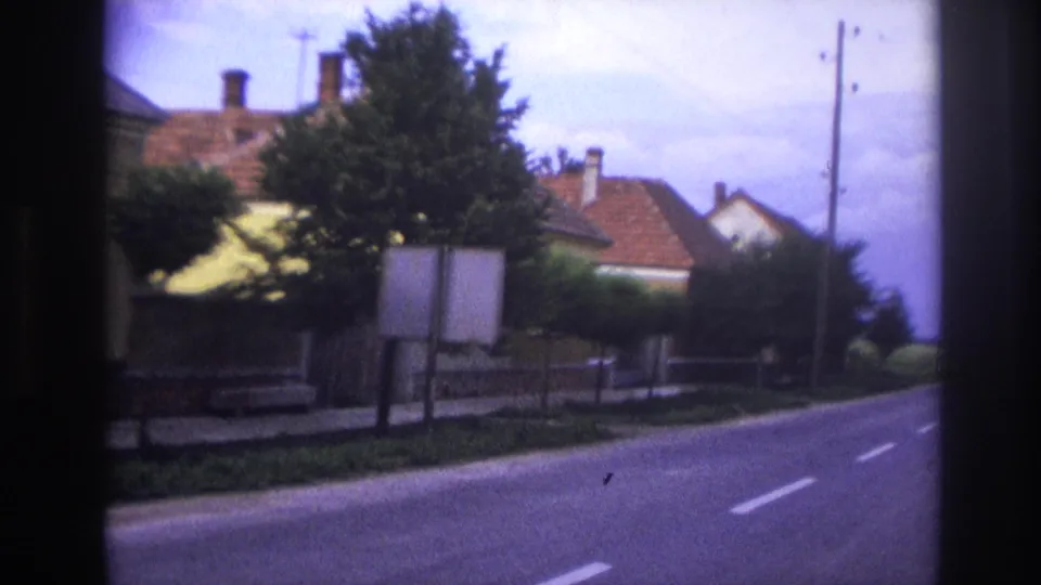 1967 France residential road view with white lane markings, roadside signs, trees, tiled-roof houses, and utility poles.