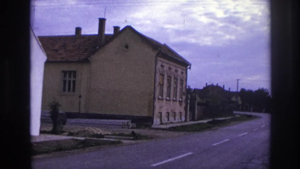 1967 France home-movie view of a roadside stucco house, chimneys, pavement, and village-edge road.