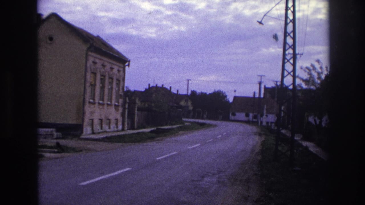 Road curving through a town with houses, utility poles, and a lattice tower.