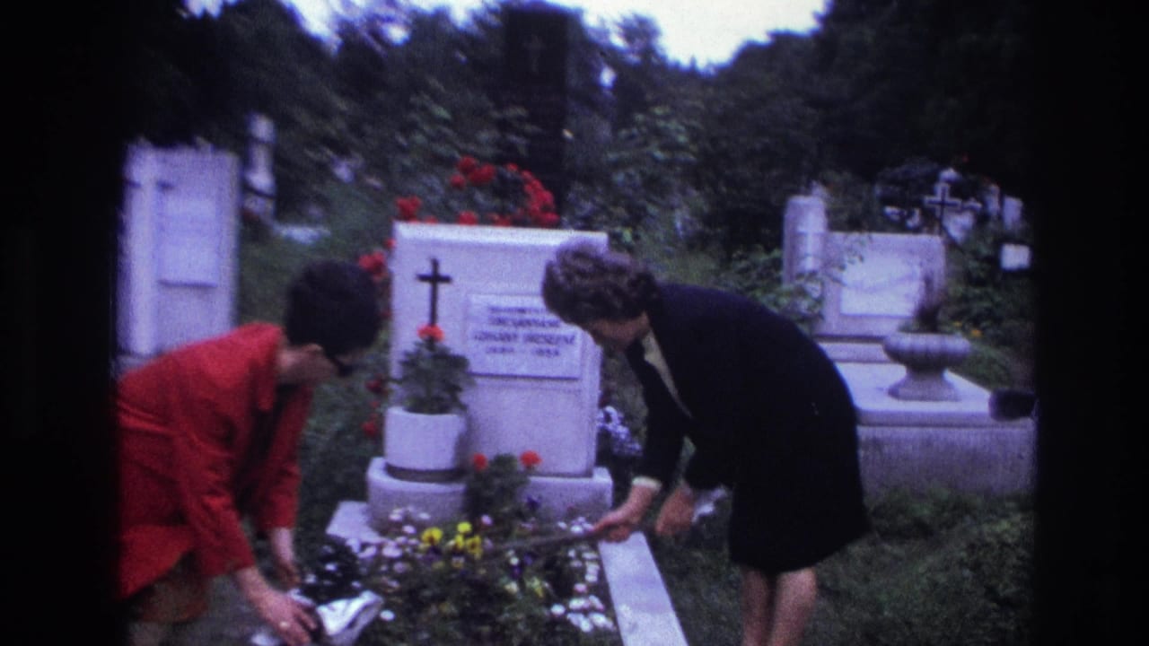 Two women bend over a grave while arranging flowers near a tombstone.