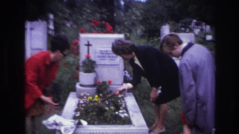 The grave-tending scene continues as a third visitor appears beside the two women arranging flowers in 1967 France.