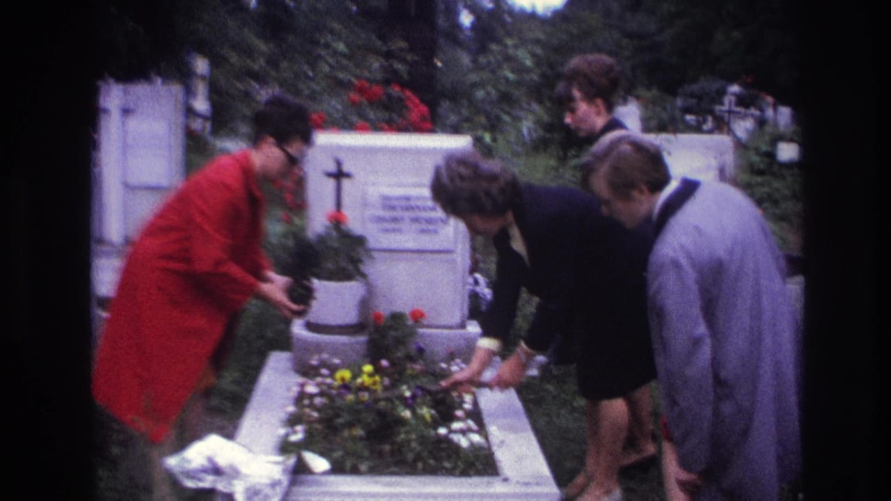 1967 France 8mm frame showing adults beside a flowered cemetery grave as a woman in a red coat bends to arrange plants.