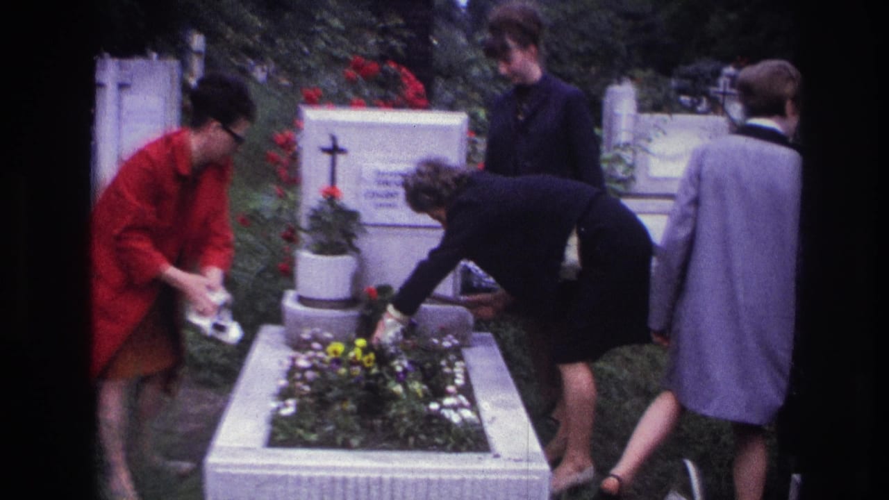In 1967 France, four women stand around a raised cemetery grave as one waters flowers and another bends over the planter.