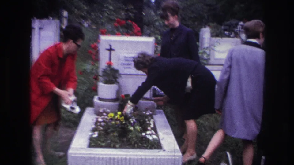 In 1967 France, four women stand around a raised cemetery grave as one waters flowers and another bends over the planter.
