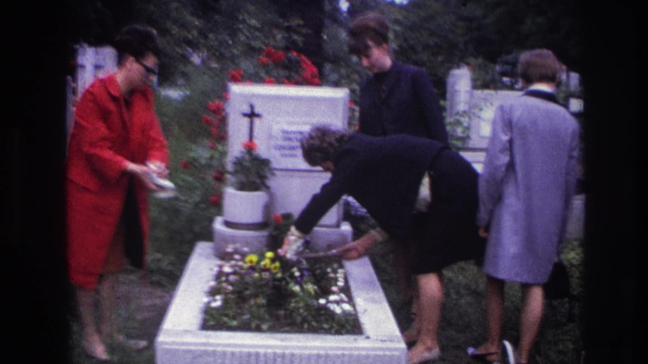 A woman in black bends over a grave planter while another holds a white container.