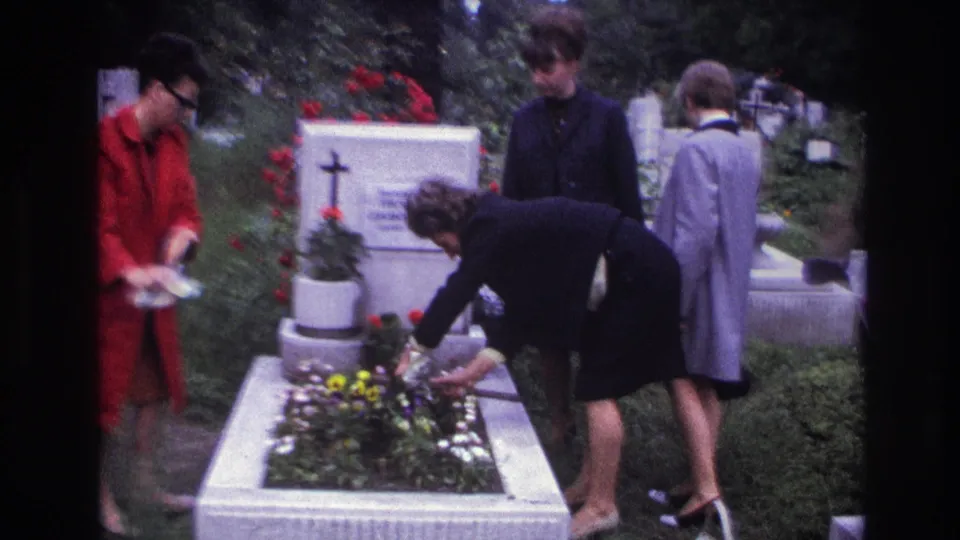 A 1967 France cemetery scene shows women quietly tending a raised grave with planted flowers and a white marker behind it.
