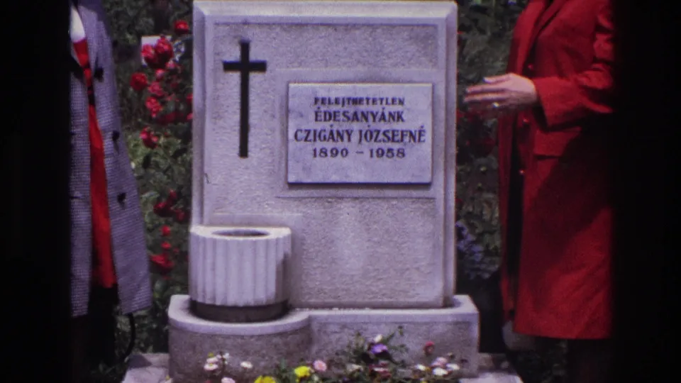 Close 1967 France cemetery view of the white stone grave with cross, readable plaque for Czigány Józsefné, flowers, and a red-coated visitor at right.