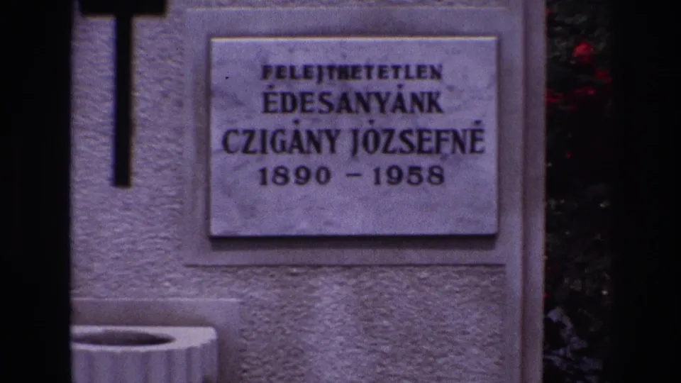 Close 8mm view of a cemetery grave marker in France, showing a black cross and Hungarian inscription for Czigany Jozsefne, 1890-1958.