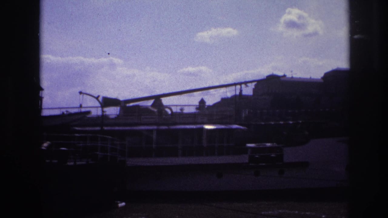 1967 France 8mm frame showing a moored riverboat below a distant waterfront skyline under a bright cloudy sky.
