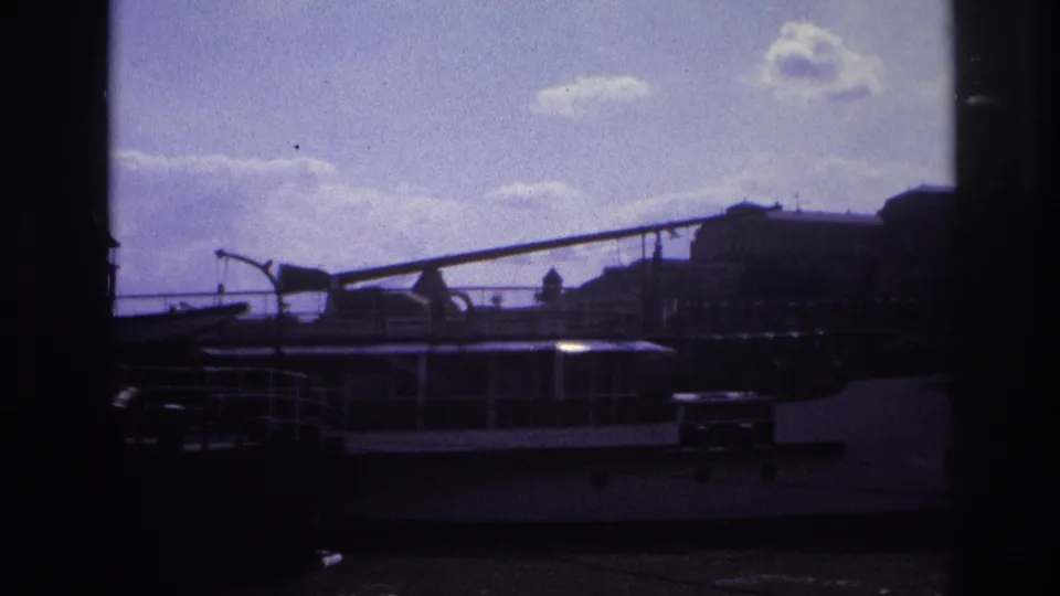 1967 France 8mm frame showing a moored riverboat below a distant waterfront skyline under a bright cloudy sky.