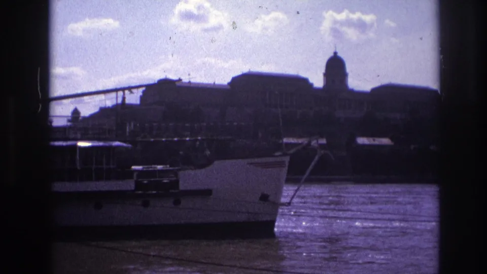 1967 France 8mm frame of a white riverboat passing a distant domed palace-like building across a bright river.