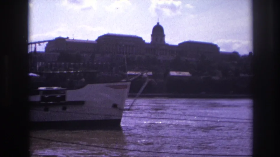 1967 France home-movie frame showing the bow of a white riverboat against a distant domed waterfront building.