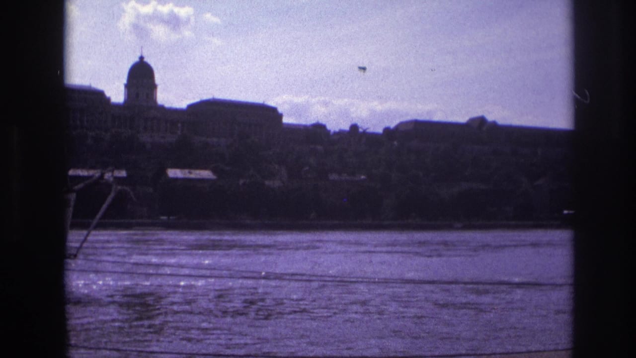 1967 France home-movie frame showing rippled river water and a domed riverside building seen through dark vertical framing.