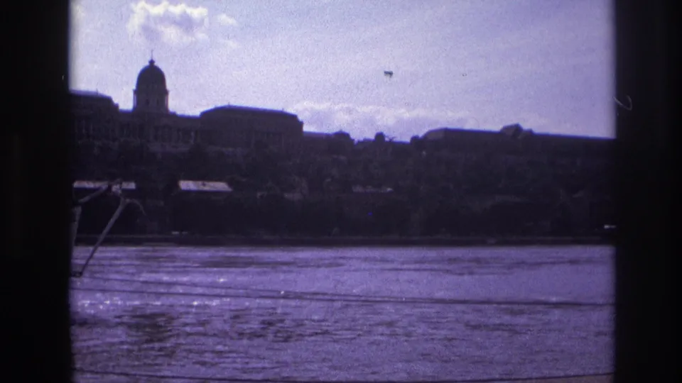 1967 France home-movie frame showing rippled river water and a domed riverside building seen through dark vertical framing.